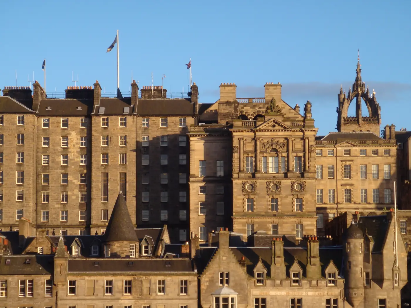 El Old Town de Edimburgo bajo el sol del atardecer visto desde el otro lado de The Mound, con altas casas de piedra superpuestas en la ladera bajo la aguja coronada de St Giles